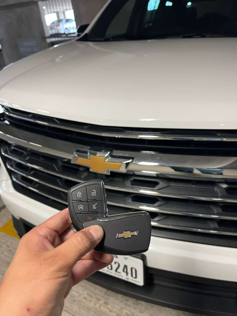 Chevrolet Tahoe key fob replacement , new 5-button smart key held up in front of white Chevy SUV, Houston TX
