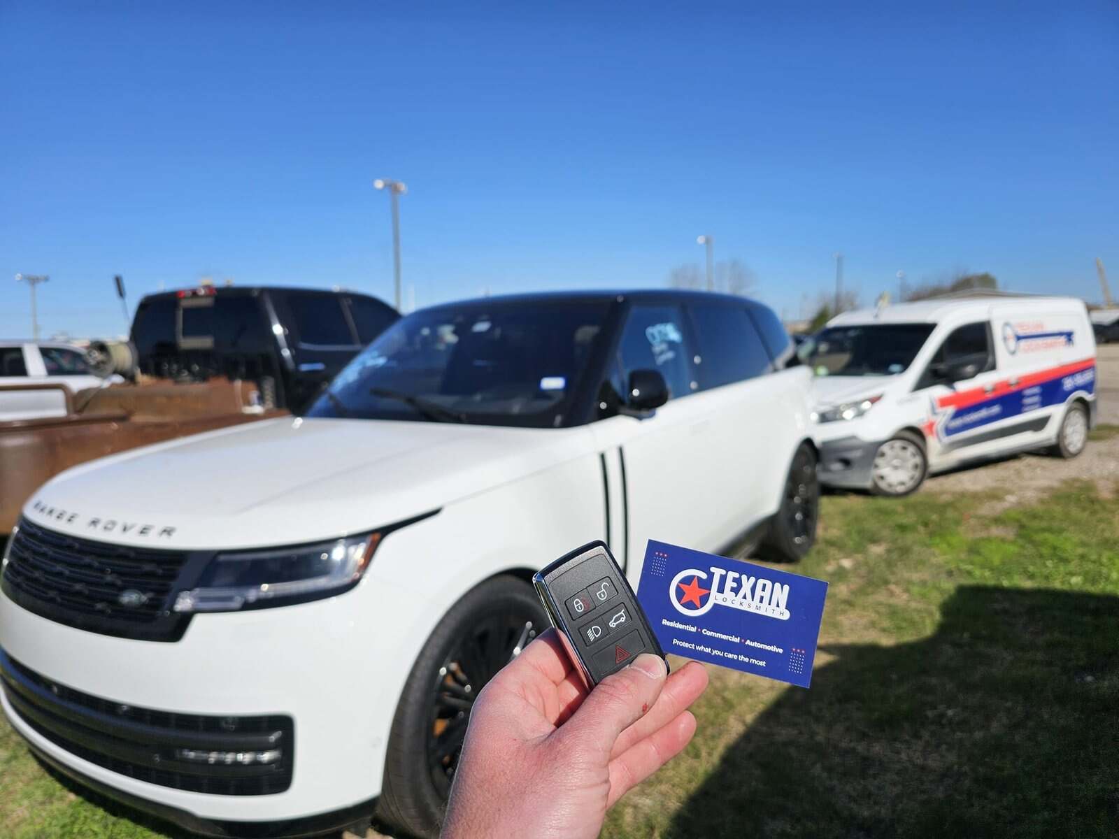 Technician holding a replacement smart key in front of a white Range Rover, with a Texan Locksmith service van parked behind it